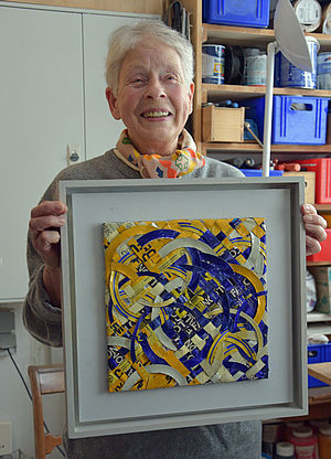 Anka Kröhnke hält einen Bilderrahmen mit einem Kunstwerk in der Hand.