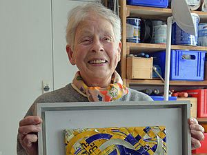 Anka Kröhnke hält einen Bilderrahmen mit einem Kunstwerk in der Hand.