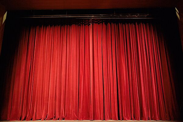 Ein geschlossener Vorhang auf einer Bühne. Der Vorhang ist rot. Die Bühne ist in einem Theater.
