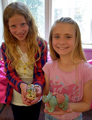 Zwei Mädchen halten bunte Nashörner aus Ton in den Händen.