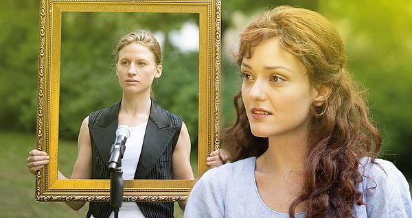 Eine junge Frau im Vordergrund. Im Hintergrund eine Frau mit einem Bilderrahmen in der Hand vor einem Mirkofon.