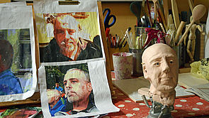 In einem Atelier hängen Porträts und steht ein Puppenkopf.