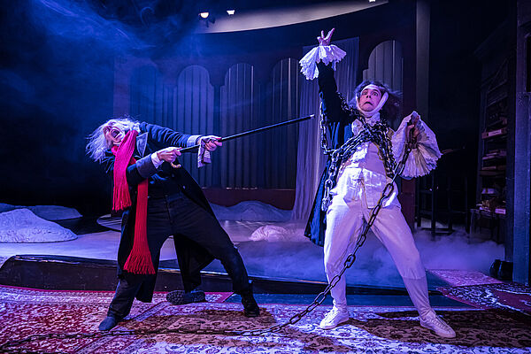 Ein Mann zieht an den Ketten eines anderen Mannes in weiß