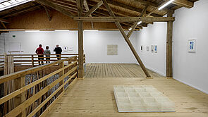 Ein heller Ausstellungsraum. Auf dem Boden liegt Kunst. An den Wänden hängen Bilder.