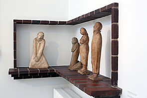Eine kniende Figur. Daneben sind drei weitere Figuren.