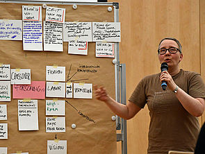 Manja Graf geht vor einer Magnettafel. An der Tafel hängen kleine Zettel mit Gedanken zum Thema "Freiraum für Visionen".