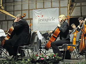 Vier Musikerinnen und Musiker sitzen auf Stühlen und spielen Kontrabass bzw. Cello.
