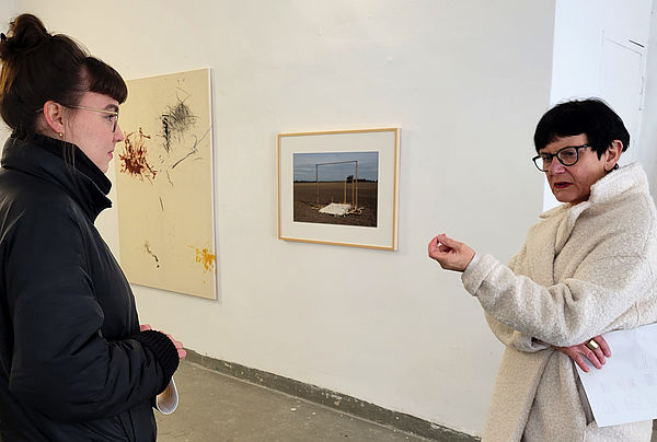 Johanna Herrmann am linken Bildrand hört eine Frau am rechten Bildrand zu. Im Hintergrund Arbeiten der Künstlerin.
