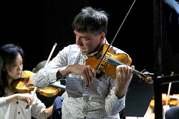 Volker Reinhold spielt eine Geige. Hinter ihm andere Musiker mit Instrumenten.