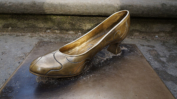 Auf einer Bronzeplatte steht ein Bronze-Schuh.