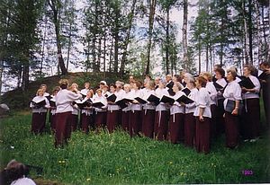 Der Chor singt draußen, auf einer Wiese, umgeben von Bäumen.