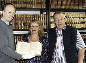 Familie Blochmann steht vor einem Regal mit historischen Büchern. Links neben ihnen steht Andreas Roloff. Er trägt weiße Handschuhe und hält die Pommernchronik aufgeschlagen in der Hand.