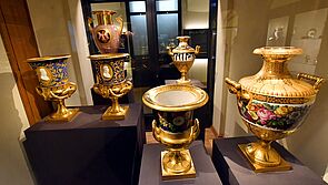In einer Vitrine stehen sechs goldene, verzierte Vasen.