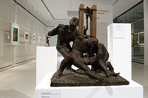 Eine dunkle Skulptur. Drei Personen sind zu erkennen.