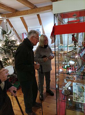 Zwei Menschen betrachten weihnachtliche Utensilien in einem Glasschrank.