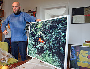 Heiko Krause hält einen großen Bilderrahmen mit einer Naturfotografie fest.