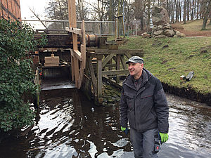 Mühlenbauer Martin Zecher steht im Wasser. Hinter ihm: die Konstruktion, die das Wasserrad hält.