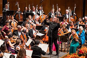 Jaap van Zweden steht dirigierend inmitten des New York Philharmonic Orchestra.