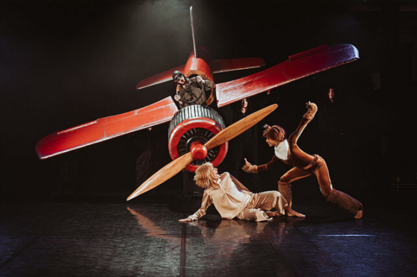 Verkleidete Schauspieler spielen auf der Bühne vor einem Doppeldecker-Flieger.