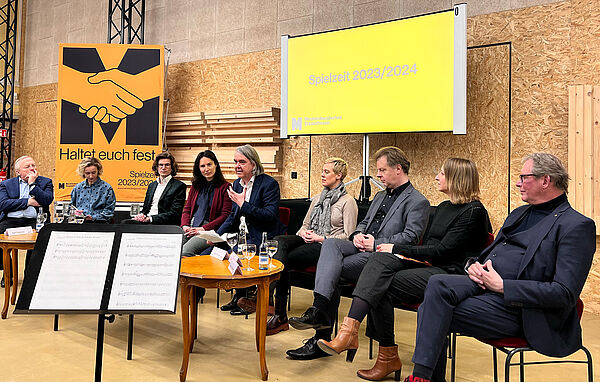 Neun Frauen und Männer sitzen nebeneinander. Hinter ihnen ein XXL-Cover des Spielzeithefts. Auf einer Leinwand steht auf gelbem Hintergrund Spielzeit 2023/2024. 