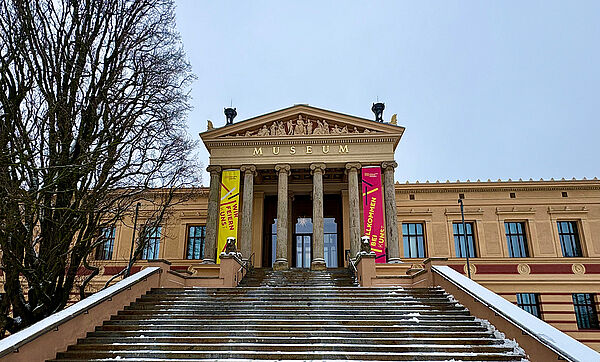 Ein Haus. Vor dem Haus sind viele Stufen. Am Ende der Stufen ist ein Eingang. Er führt ins Museum.