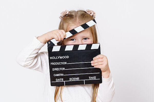 Ein Mädchen hält eine Filmklappe vor sich. 