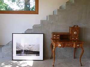An einer grauen Treppe lehnt ein schwarzer Bilderrahmen mit einer Schwarz-Weiß-Fotografie.