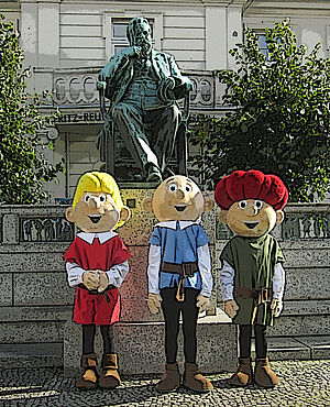 Drei Menschen stehen als Abrafaxe verkleidet vor dem Fritz-Reuter-Denkmal in Stavenhagen.