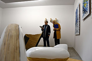 Zwei Frauen zeigen auf Kunstarbeiten, von denen sie umgeben sind.