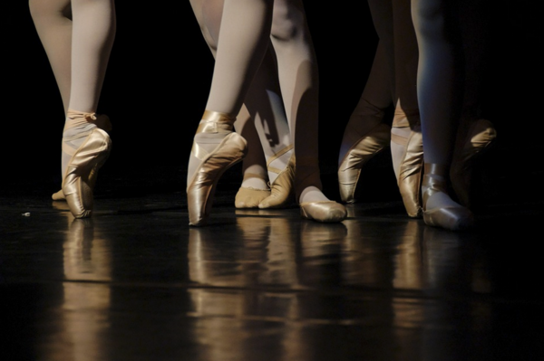 Zu sehen sind die Beine von Tänzerinnen. Sie tragen Ballettschuhe.