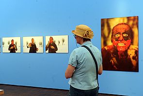 Ein Mann steht vor einer blauen Wand, an der vier Bilder hängen.