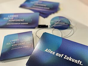 Auf einem Tisch liegen Karten und Flyer zur Kulturkonferenz. Auf einer Karte steht „Alles auf Zukunft“. 