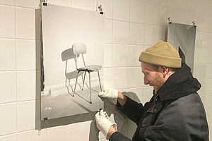 Steffen Stender hängt eines seiner Bilder - eine Schwarz-Weiß-Aufnahme von einem alten Stuhl - an die Wand. 