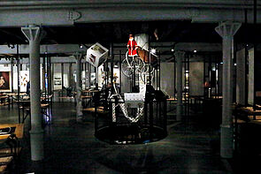 Blick in den Ausstellungsraum. Ein Kinderwagen hängt an der Decke.