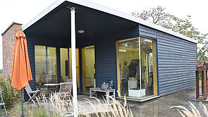 Ein blauer Holzbungalow mit großen Fenstern und überdachter Terrasse.