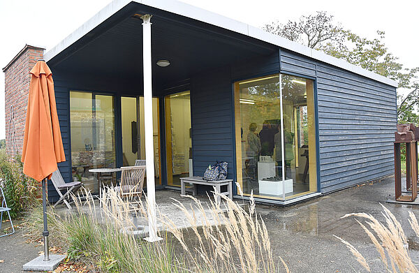 Ein blauer Holzbungalow mit großen Fenstern und überdachter Terrasse.