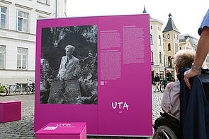 Eine Frau in einer schwarz-weiß Fotografie auf magenta-farbener Wand.