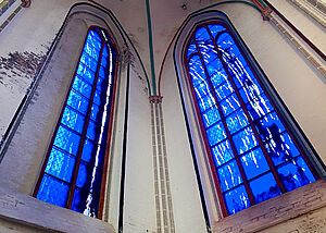 Zwei hohe Kirchenfenster mit blau-weiß schattiertem Glas.