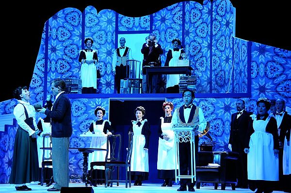 Der Querschnitt eines Hauses. In der oberen und unteren Etage stehen Dienstmädchen und Butler. Sie singen.