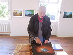 Volkmar Herre hat eine Fotografie vor sich auf dem Tisch und zeigt mit dem Finger drauf.