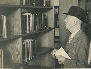 Ein Mann steht vor einem Bücherregal und sucht ein Buch. Schwarz-Weiß-Aufnahme.