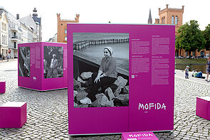 Eine Frau mit Kopftuch sitzt auf den Steinen einer Hafenmauer.