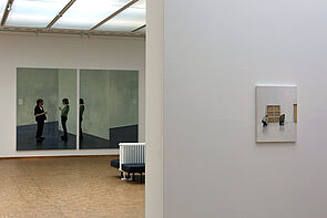 Ein Blick in die Ausstellung. Das Gemälde hinten zeigt zwei Frauen, die miteinander sprechen.