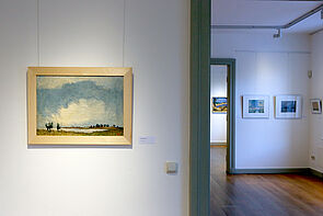Ein Landschaftsbild. Im Hintergrund zu sehen: weitere Ausstellungsräume.