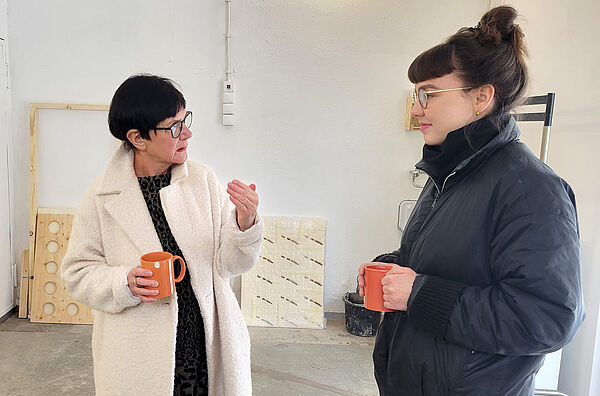 Eine Frau spricht mit Künstlerin Johanna Herrmann. im Hintergrund lehnen Arbeiten an der Wand.