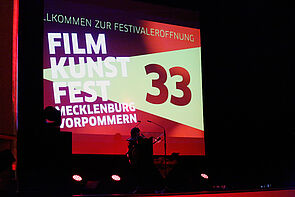 Blick auf die Bühne. Auf der Leinwand ist das Plakat des Filmkunstfestes zu sehen.