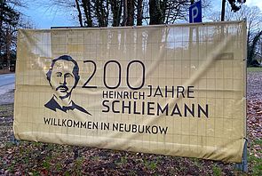 Ein Banner weist in Neubukow am Straßenrand auf den 200. Geburtstag von Schliemann hin.
