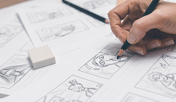 Eine Hand malt mit einem Bleistift Comics.