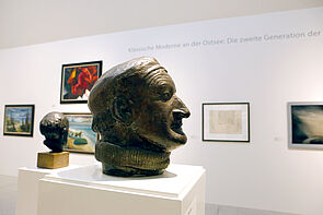 Der Kopf eines älteren Mannes als Büste. im Hintergrund hängen Bilder.