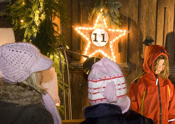 Drei Kinder stehen in Mütze und dicken Jacken draußen. Im Hintergrund leuchtet ein Stern. Er trägt die Nummer 11.